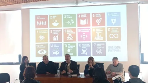 Panel de expositores frente a una proyección con los 17 Objetivos de Desarrollo Sostenible.