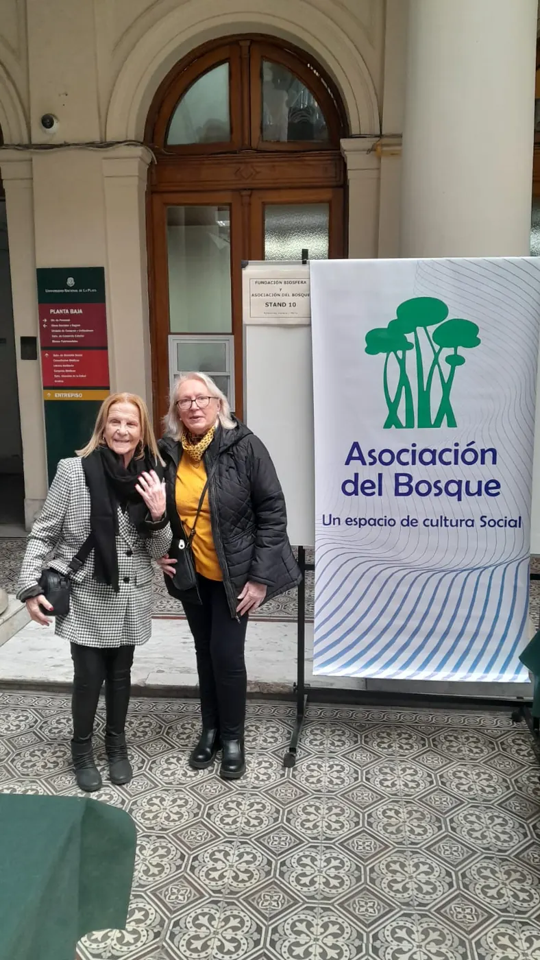 Dos participantes junto al banner de la Asociación del Bosque en la entrada de la muestra.