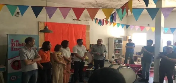 Encuentro en una biblioteca popular: el público de pie en un salón decorado con banderines de colores.
