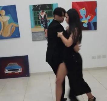 Una pareja baila tango en una sala con pinturas expuestas en las paredes.
