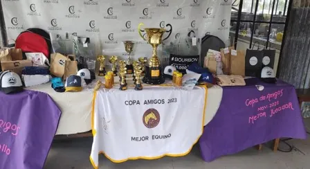 Mesa de premios con trofeos y gorras junto a la bandera de la Copa Amigos 2023 al mejor equipo.
