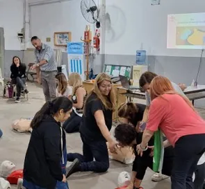 Un instructor guía a los participantes que practican RCP en el piso de un salón.