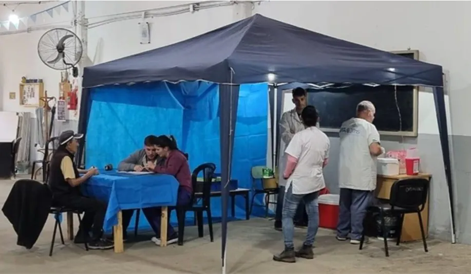 Puesto de atención sanitaria bajo un gazebo azul, con profesionales atendiendo a vecinos.